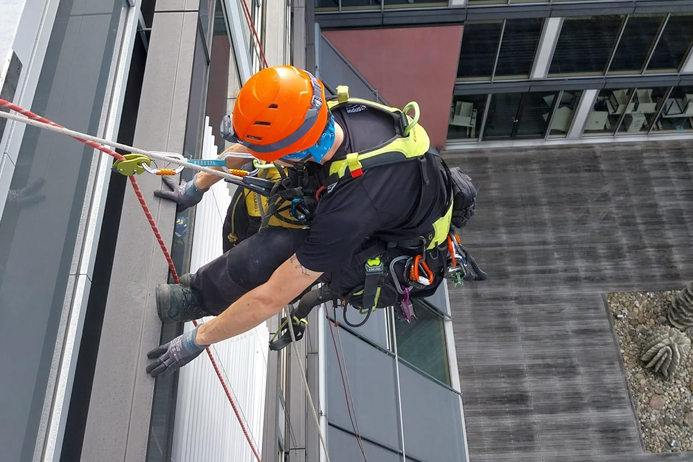 Handwerker seilt sich ab um eine Sonnenschutzanlage zu reparieren.