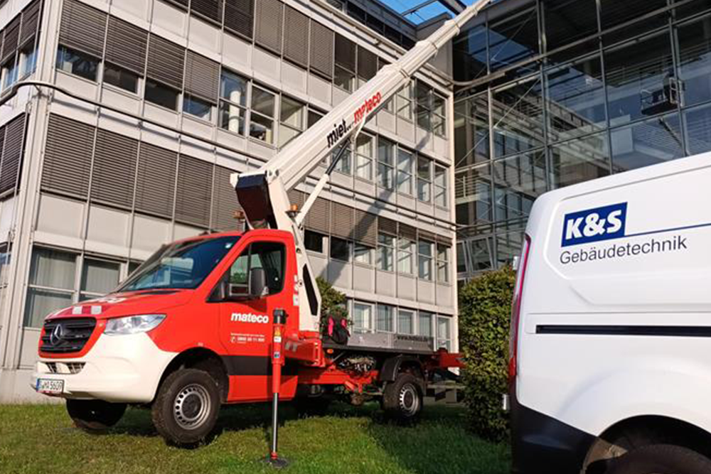 Hubsteigwagen mit ausgefahrenem Kranarm vor einem Gebäude, daneben ein K&S Gebäudetechnik Lieferwagen